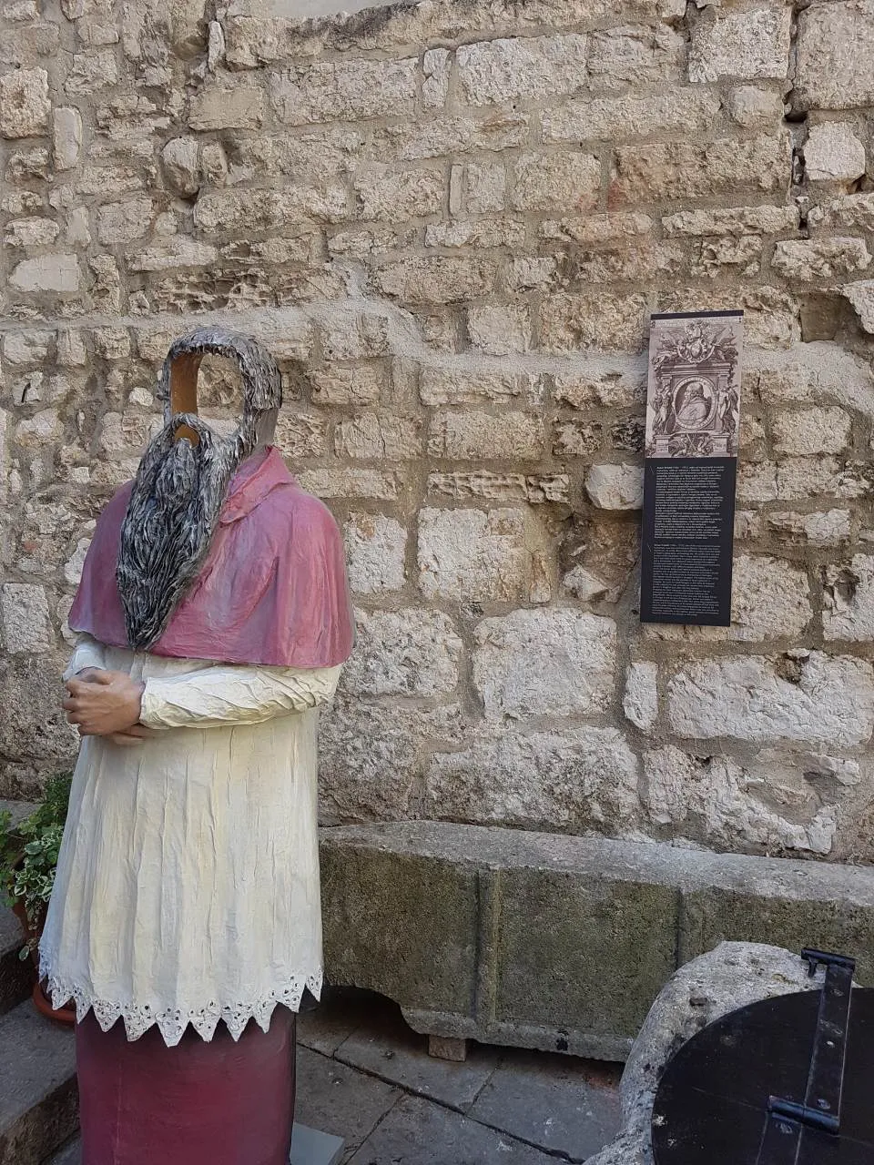 Exhibition display with an information plate against a stone wall in Šibenik